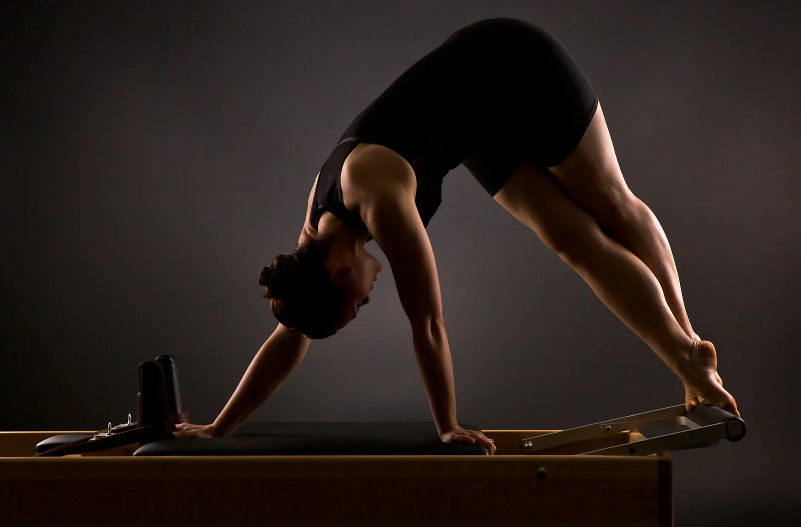 Mujer practicando Pilates Reformer en un estudio de luz tenue